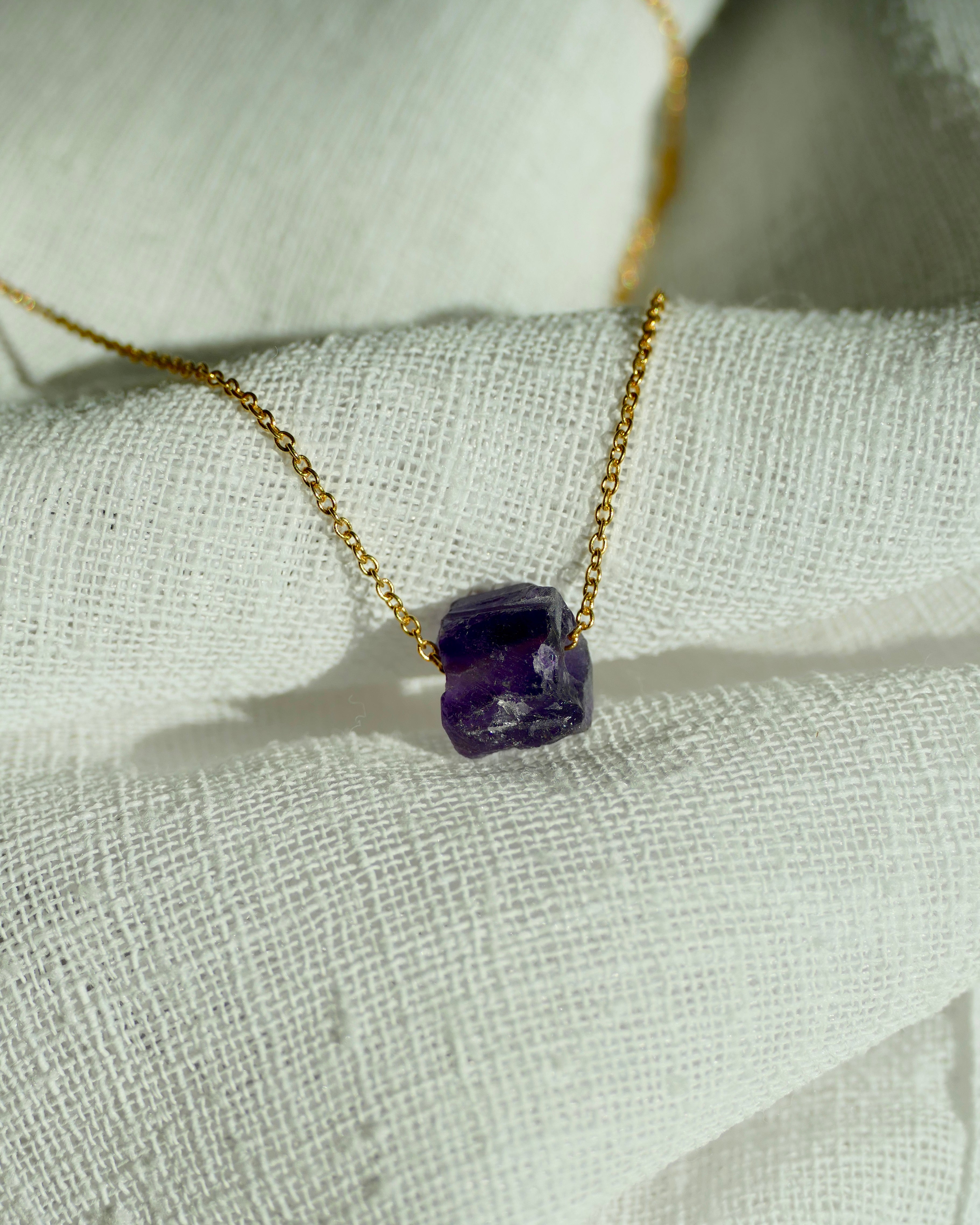 Necklace with a purple gemstone pendant on a light fabric background