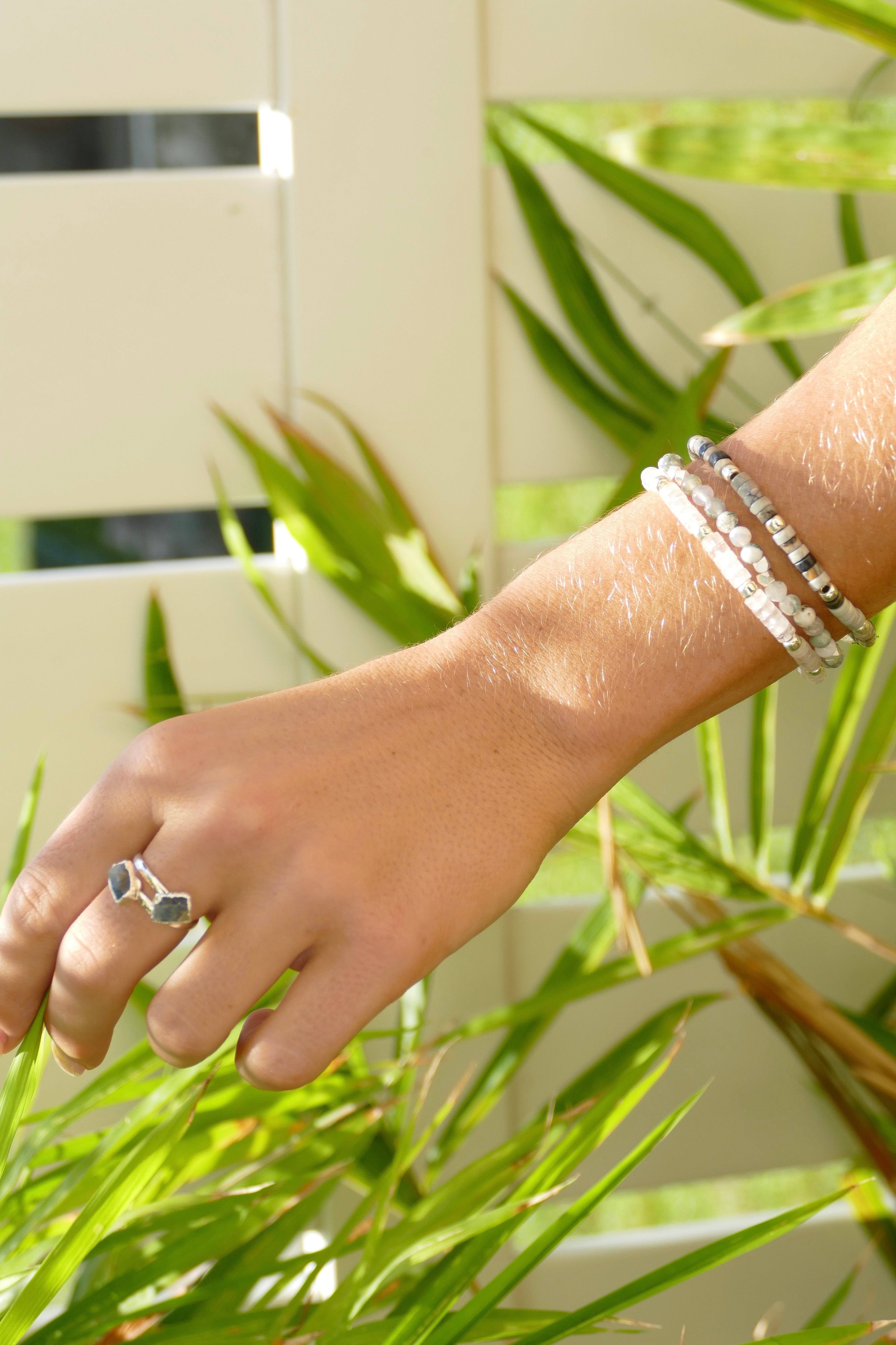 Model wearing adjustable gemstone ring and heishi stack bracelets