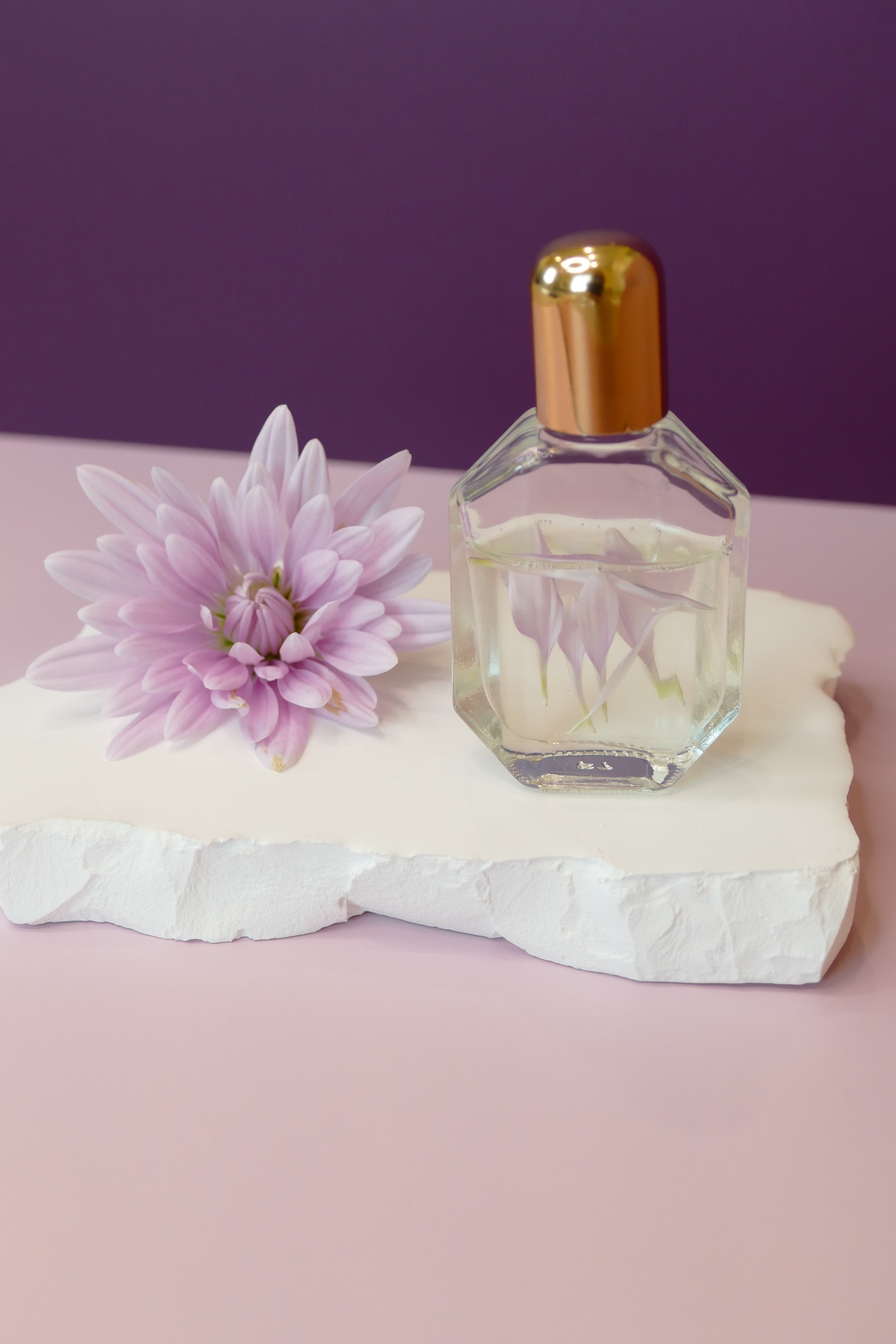 Purple background with flower and glass roller bottle.