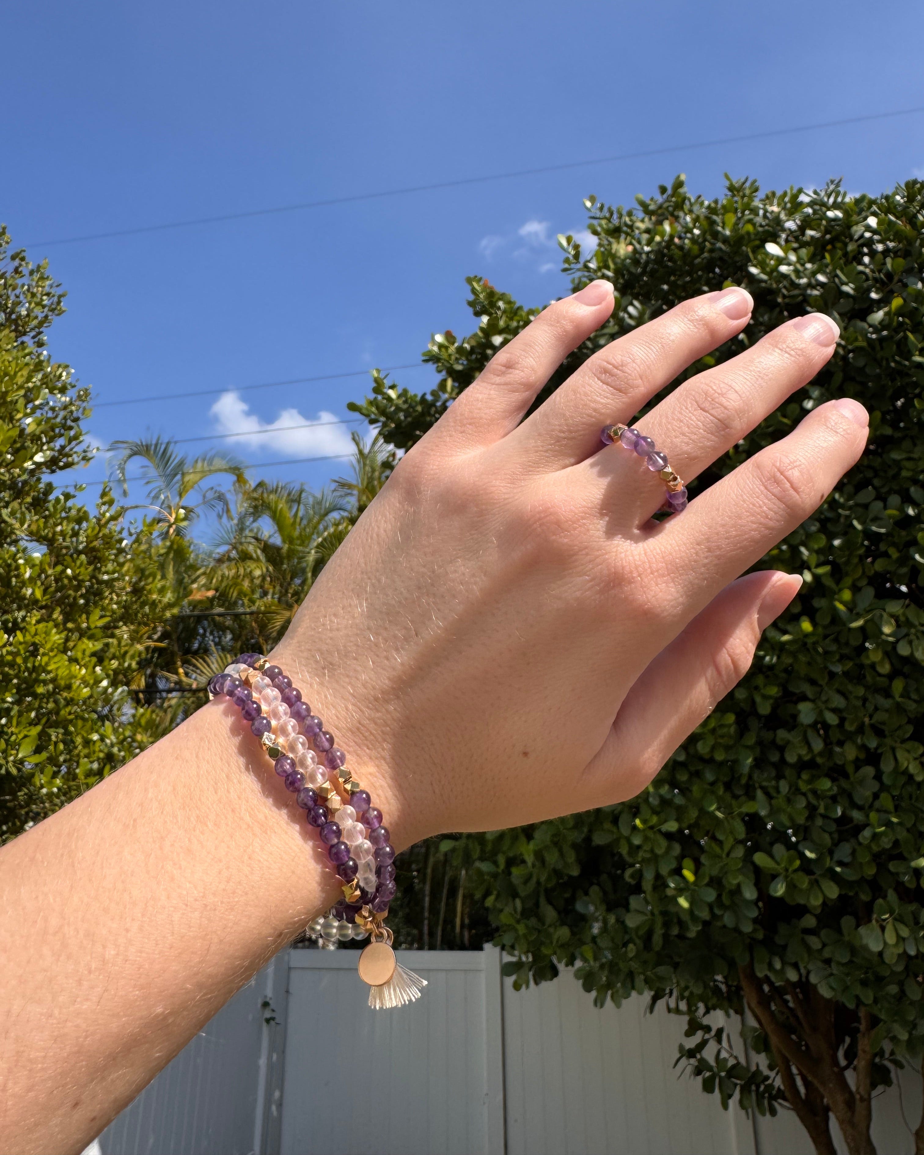 Hand wearing a bracelet with a clear blue sky and trees in the background